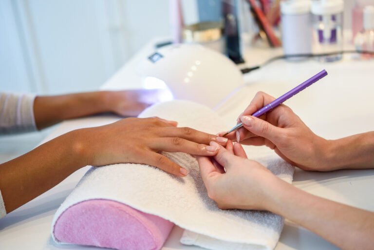 Close-up of beautician painting a woman's nails with a brush in a nail salon. Costumer receiving a manicure.